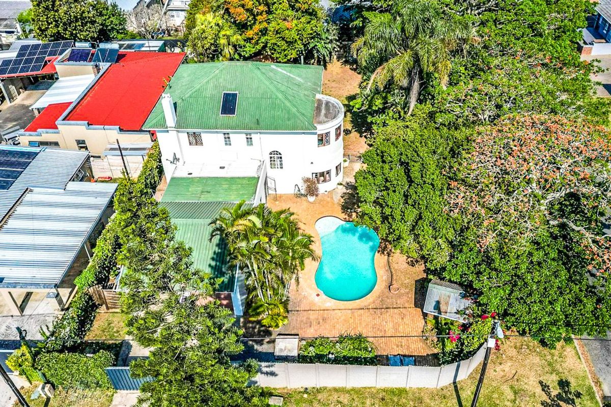 Aerial view of the property featuring a swimming pool, brick paved patio area, and a multi-level house with a green metal roof.