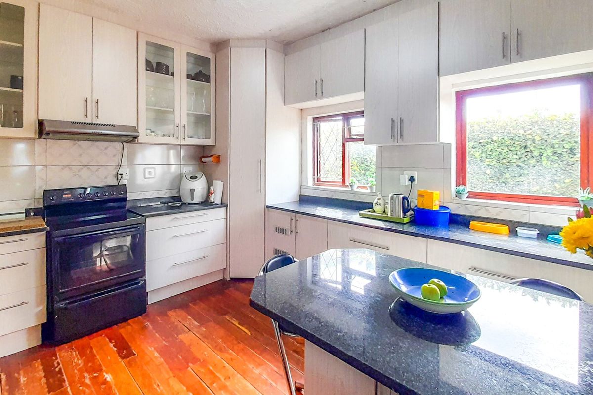 A functional kitchen featuring white cabinetry, dark granite countertops, a tiled backsplash, and timber flooring with natural light from dual windows.