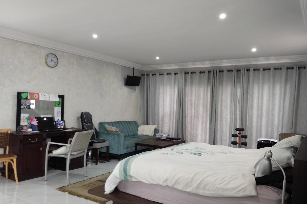 Spacious bedroom featuring tiled flooring, recessed ceiling lighting, and large sliding glass doors with floor-to-ceiling curtains providing natural light.