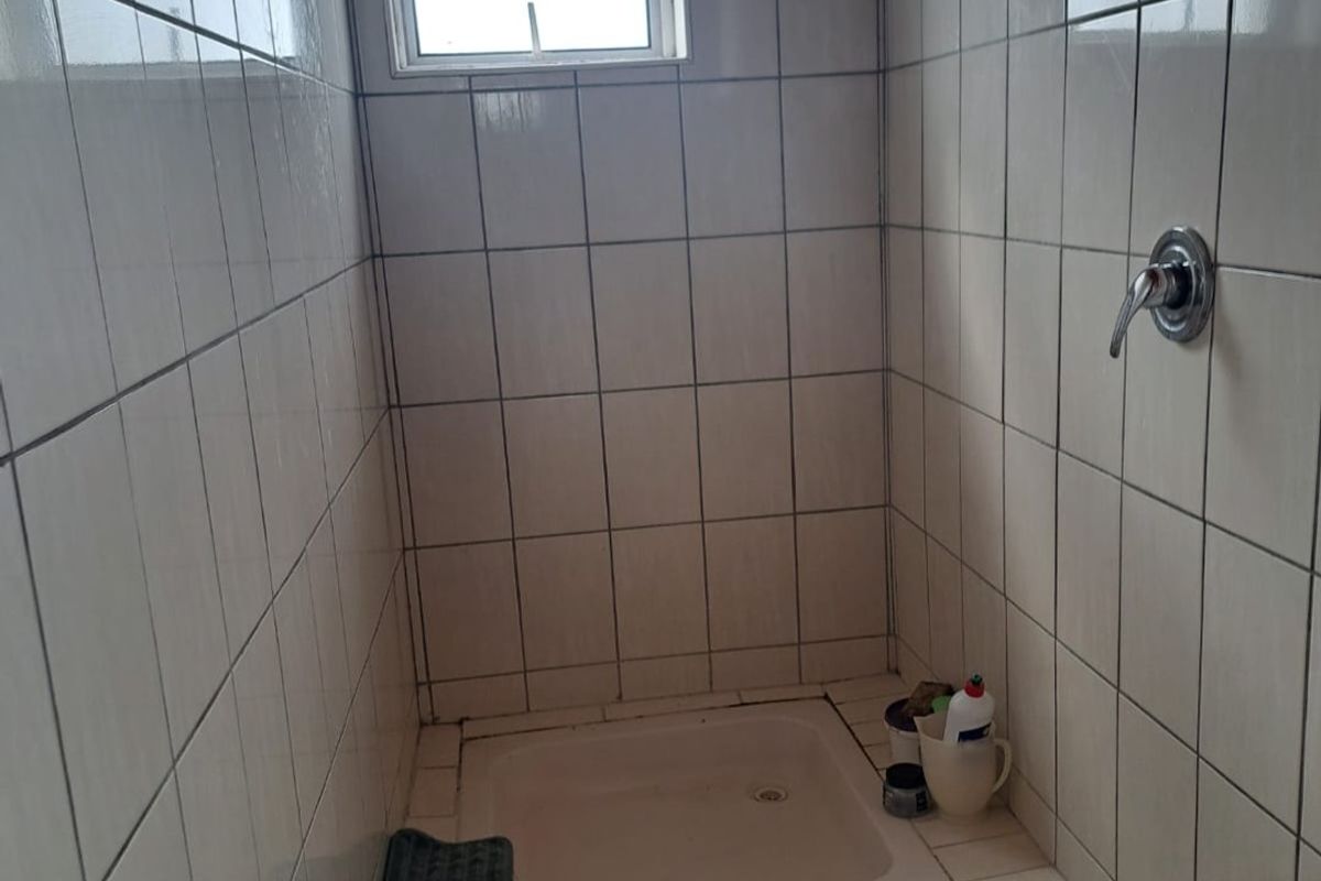 A compact shower enclosure featuring tiled walls and flooring, a raised shower base, and a wall-mounted shower mixer.
