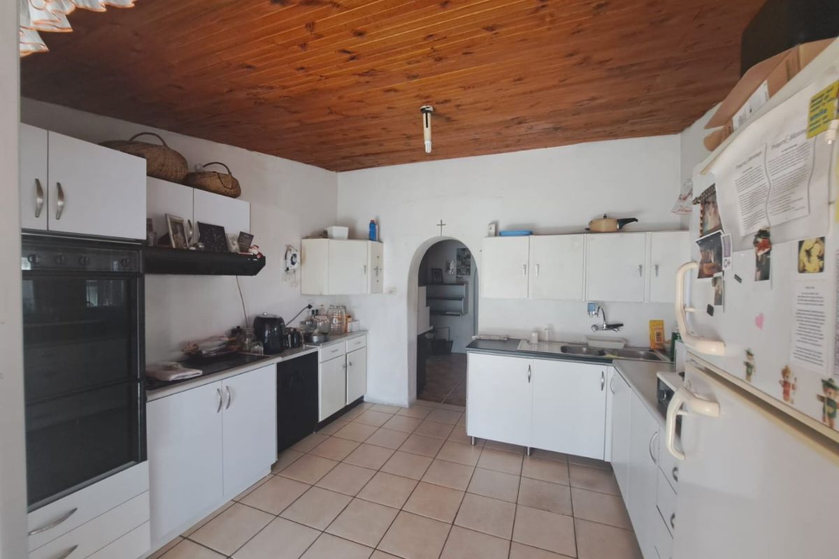 A functional kitchen featuring white built-in cabinetry, a built-in oven, hob, and a distinctive timber-clad ceiling with tiled flooring.