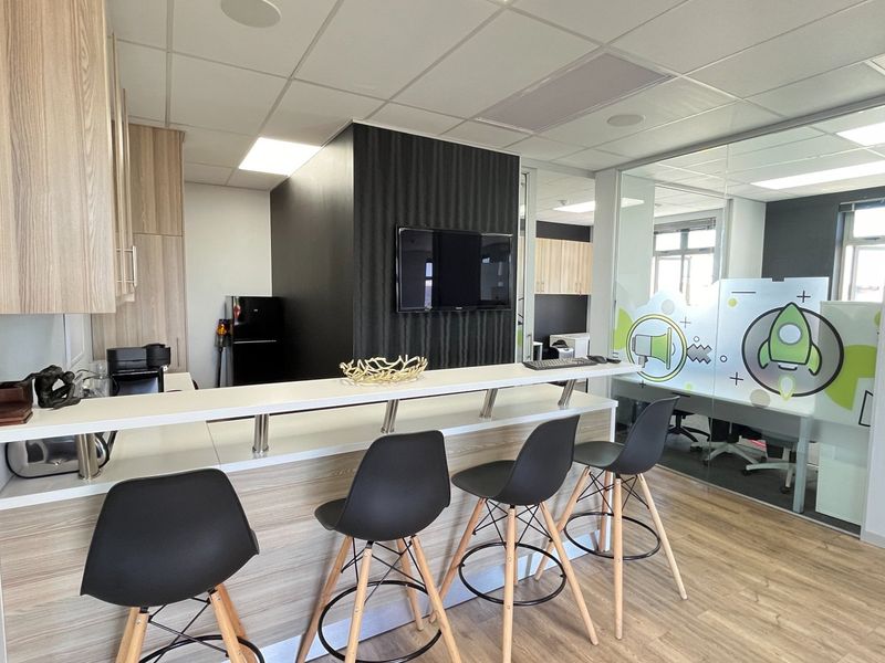 Modern open-plan commercial office space featuring a breakfast bar, laminate flooring, and a glass-partitioned meeting room with contemporary finishes.
