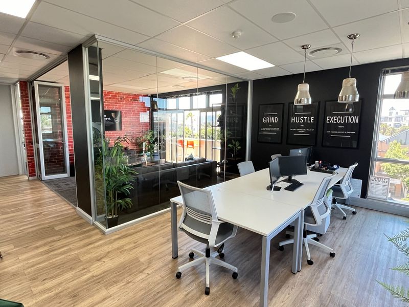 Modern commercial office space featuring a glass-partitioned meeting area, wood-look laminate flooring, and an exposed brick feature wall with ample natural light.