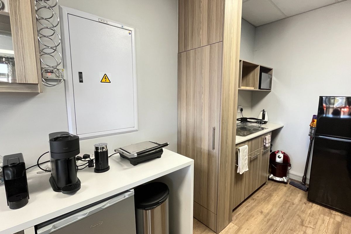 A compact commercial kitchenette featuring modern wood-look cabinetry, laminate countertops, and a dedicated electrical distribution board.