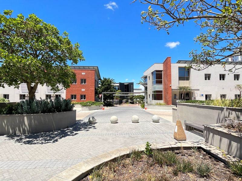 A well-maintained commercial office park entrance featuring paved driveways, landscaped garden beds, and modern brick and concrete building facades.