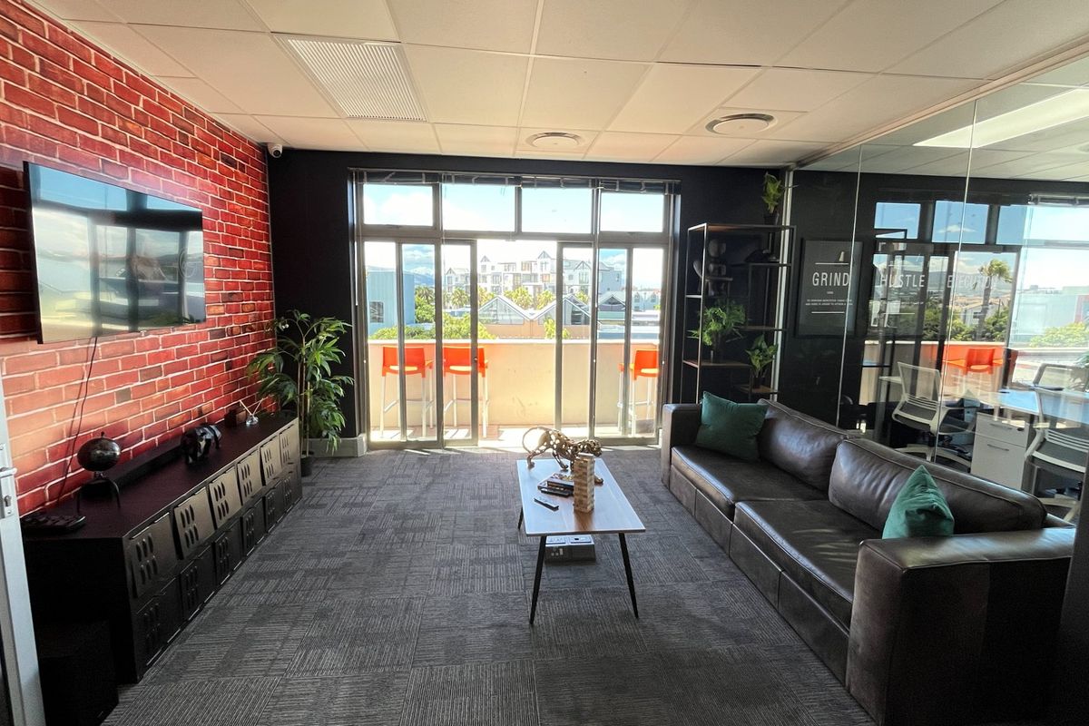 Modern commercial lounge area featuring a brick-effect feature wall, suspended ceiling, and glass partition walls, offering access to an outdoor balcony.
