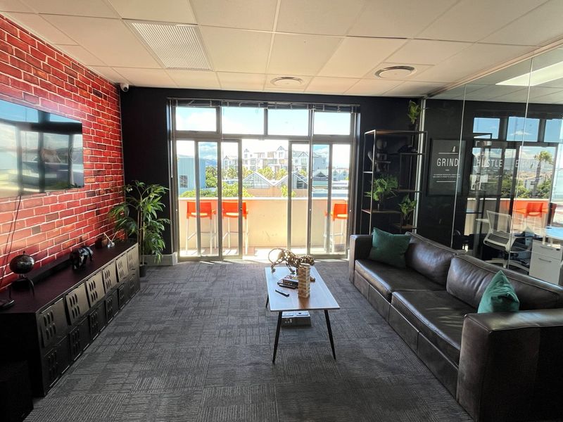 Modern commercial lounge area featuring a brick-effect feature wall, suspended ceiling, and glass partition walls, offering access to an outdoor balcony.