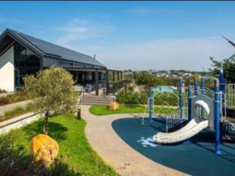 A well-maintained communal garden area featuring a modern playground, paved pathways, and landscaped surroundings adjacent to a contemporary building.