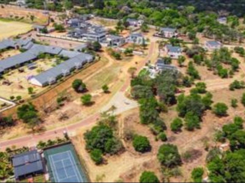 Aerial view of a residential estate featuring paved roads, established vegetation, and a tennis court within a landscaped community setting.