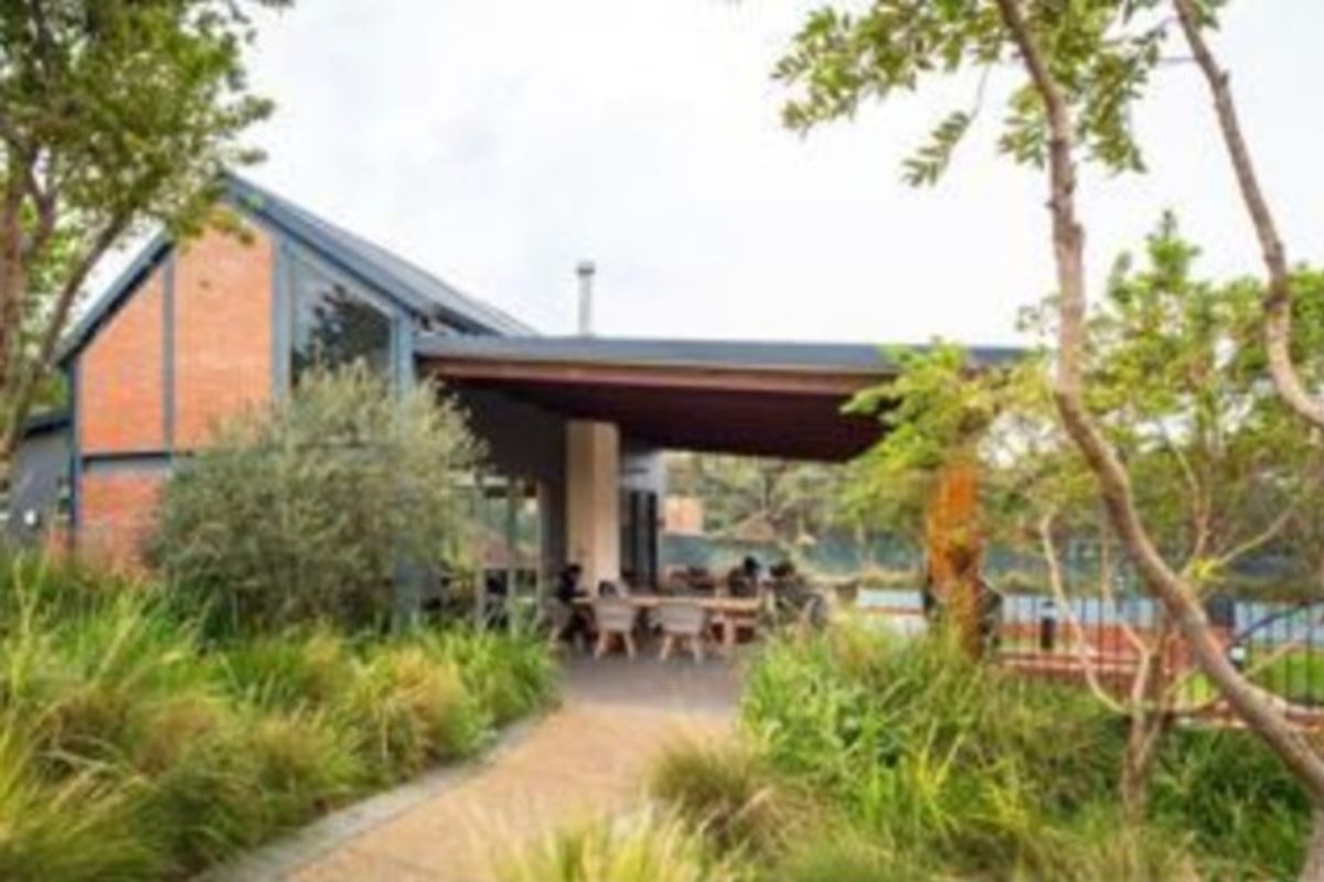 A view of the rear exterior featuring a covered patio area, exposed brick architecture, and a well-maintained landscaped garden with a paved pathway.