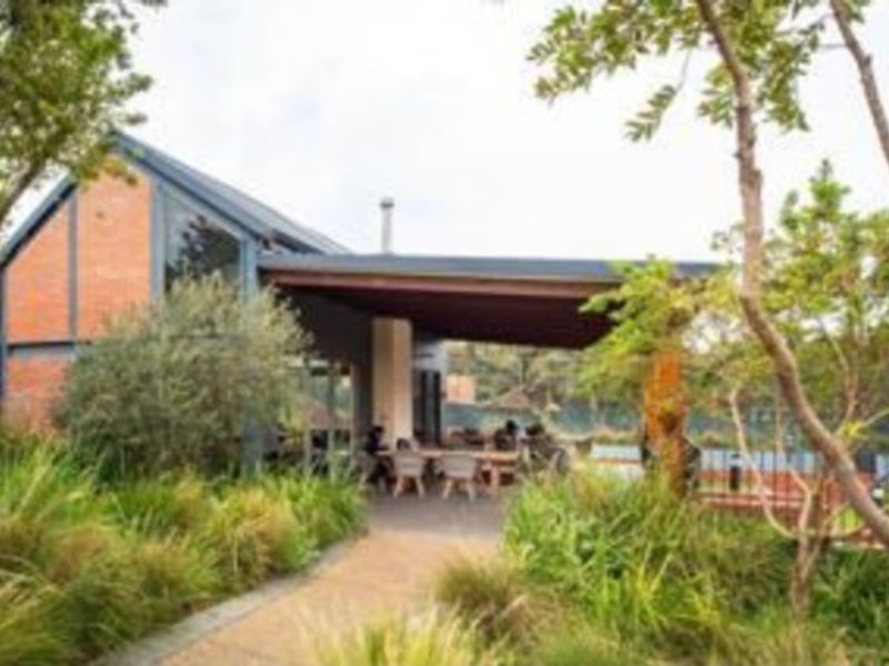 A view of the rear exterior featuring a covered patio area, exposed brick architecture, and a well-maintained landscaped garden with a paved pathway.
