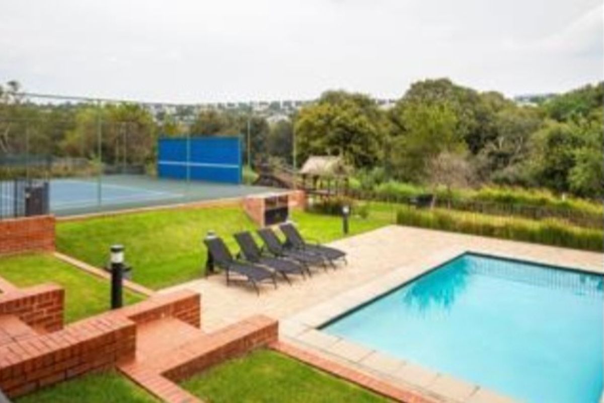 Outdoor recreational area featuring a swimming pool, paved deck, built-in braai, and a private tennis court set within a landscaped garden.