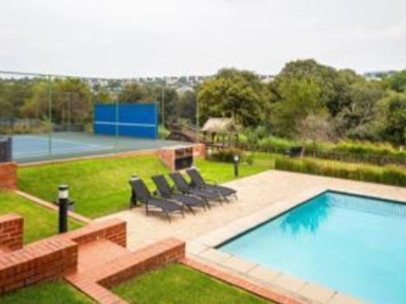Outdoor recreational area featuring a swimming pool, paved deck, built-in braai, and a private tennis court set within a landscaped garden.