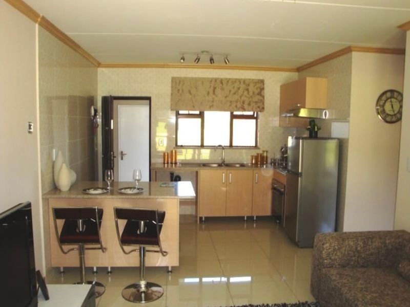 An open-plan kitchen and living area featuring light wood cabinetry, a breakfast counter, tiled flooring, and integrated kitchen appliances.