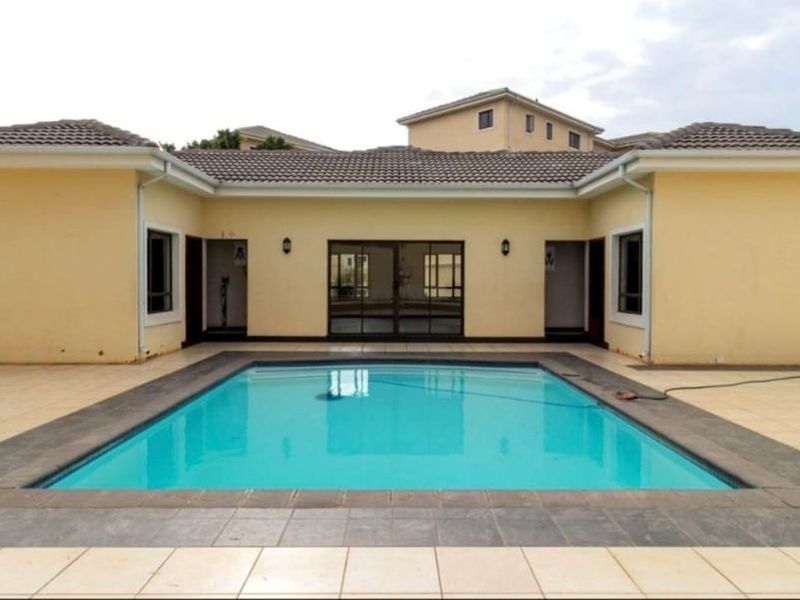 A rear exterior view featuring a swimming pool set within a paved patio area, surrounded by the property's main structure with sliding door access.