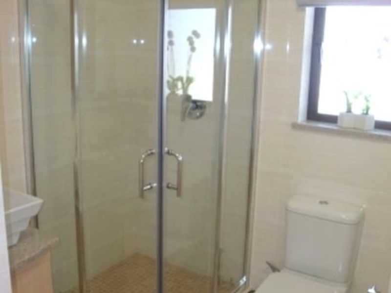 A functional bathroom featuring a corner shower enclosure, a standard toilet, and a vanity cabinet with tiled walls and flooring.