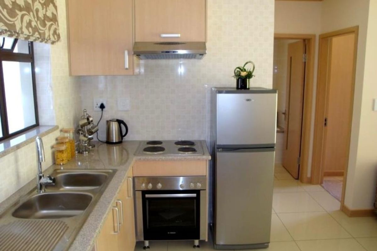 A compact, functional kitchen featuring light wood cabinetry, granite countertops, stainless steel sink, and built-in oven with hob and extractor fan.