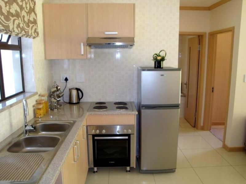 A compact, functional kitchen featuring light wood cabinetry, granite countertops, stainless steel sink, and built-in oven with hob and extractor fan.