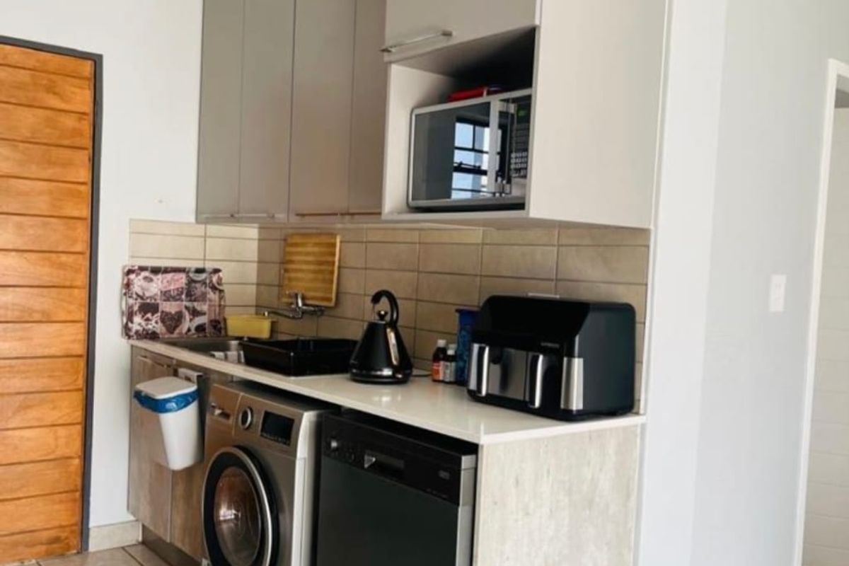 Compact kitchen area featuring modern built-in cabinetry, tiled backsplash, and integrated appliance spaces, finished with neutral tiled flooring.