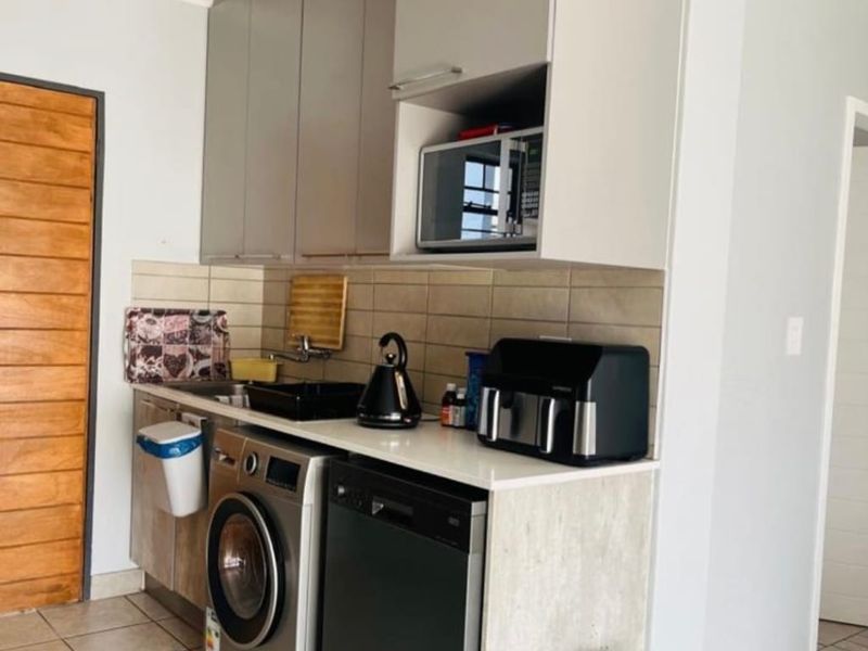 Compact kitchen area featuring modern built-in cabinetry, tiled backsplash, and integrated appliance spaces, finished with neutral tiled flooring.