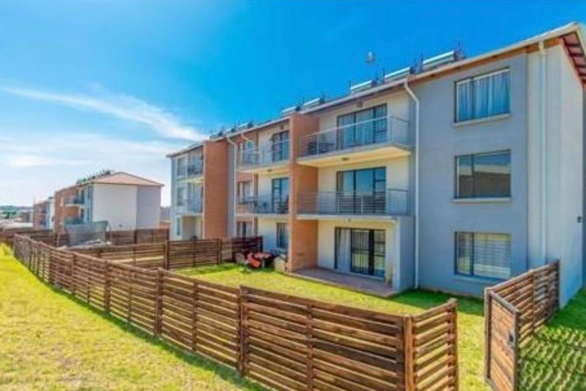 Rear view of a multi-story apartment complex featuring private balconies, ground-floor patios, and enclosed garden areas with timber fencing.