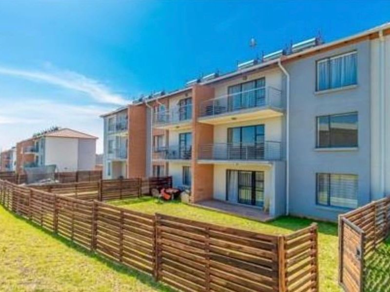 Rear view of a multi-story apartment complex featuring private balconies, ground-floor patios, and enclosed garden areas with timber fencing.