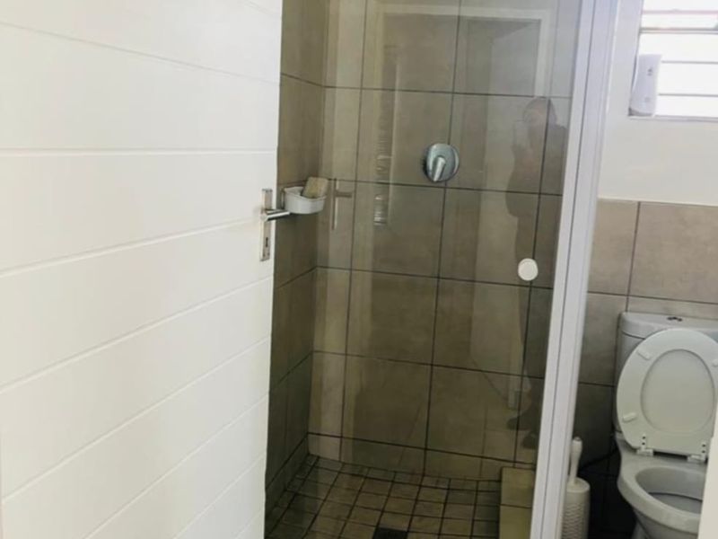 A functional bathroom featuring a tiled shower enclosure with a glass door, a standard toilet, and tiled finishes throughout.
