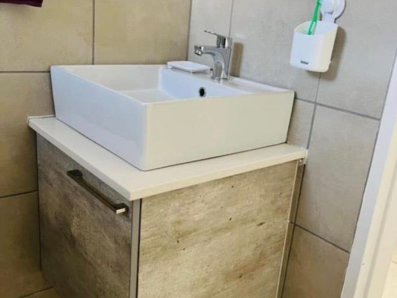 A modern bathroom vanity featuring a wall-mounted cabinet, white vessel sink, and chrome mixer tap, complemented by neutral ceramic wall and floor tiling.