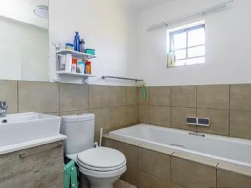A functional bathroom featuring a vanity cabinet with a basin, a standard toilet, and a tiled bathtub area with neutral wall tiles.