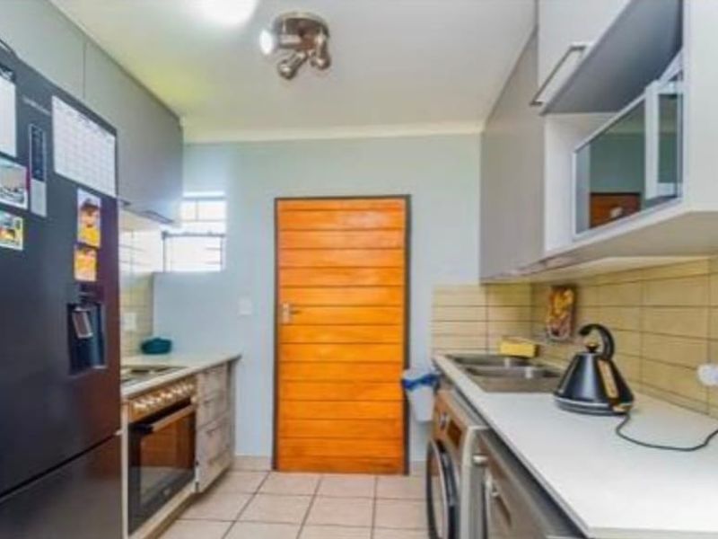 A functional kitchen featuring built-in cabinetry, tiled backsplash, integrated oven and hob, and tiled flooring with a rear access door.