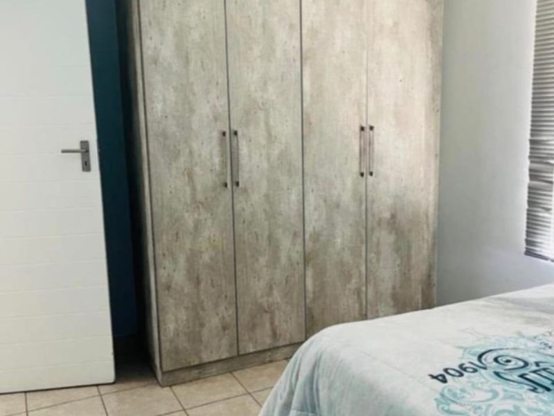 A bedroom featuring a large built-in wardrobe with a wood-look finish, tiled flooring, and window blinds.
