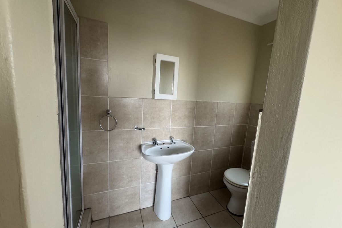 A functional bathroom featuring a pedestal basin, shower enclosure, and toilet with neutral wall and floor tiling.