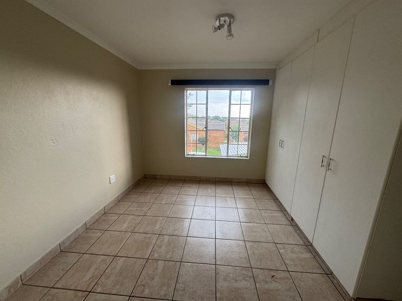 An empty bedroom featuring tiled flooring, built-in cupboards, and a window with security bars, offering a neutral canvas for personalization.
