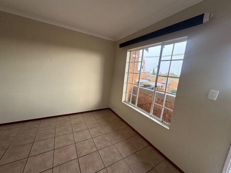 An empty bedroom featuring tiled flooring, a window with security bars, and a roller blind, offering a neutral space ready for personalization.