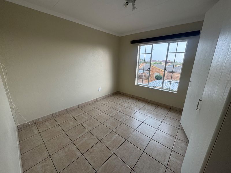 A clean, empty bedroom featuring neutral wall paint, tiled flooring, and a built-in wardrobe, offering a blank canvas for personalization.