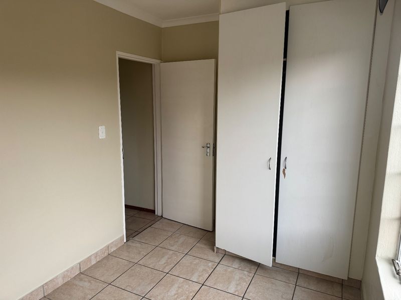 A vacant bedroom featuring neutral wall paint, tiled flooring, and built-in cupboards, offering a clean and functional space ready for personalization.
