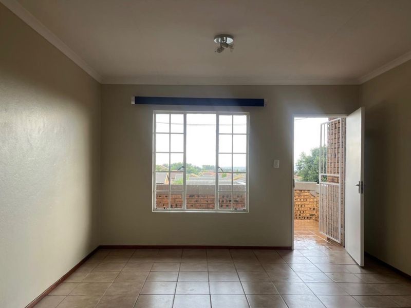 An empty, neutrally painted living room featuring tiled flooring, a large window with security bars, and direct access to an outdoor balcony area.