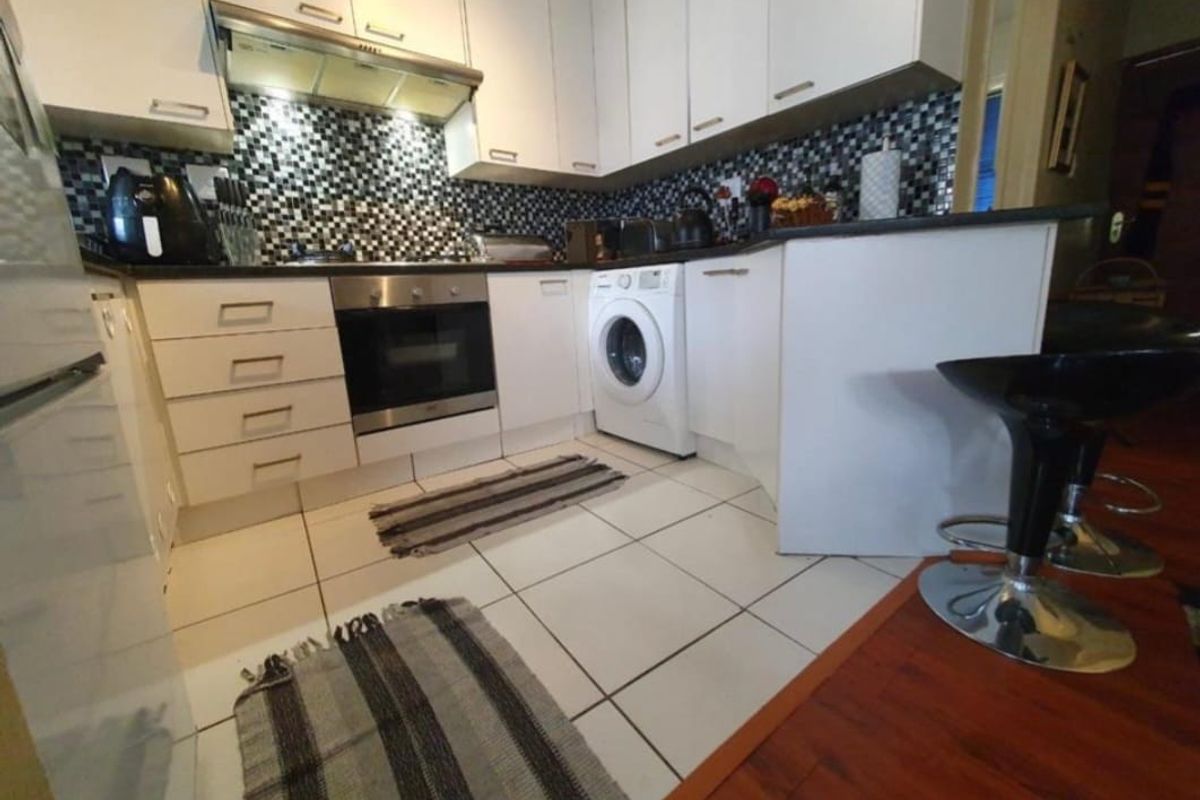 Compact kitchen featuring white cabinetry, mosaic tile backsplash, integrated oven, extractor fan, and a built-in washing machine with tiled flooring.