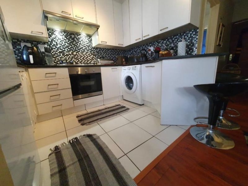 Compact kitchen featuring white cabinetry, mosaic tile backsplash, integrated oven, extractor fan, and a built-in washing machine with tiled flooring.