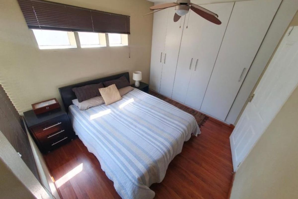 A bedroom featuring laminate flooring, built-in cupboards, a ceiling fan, and horizontal window blinds.
