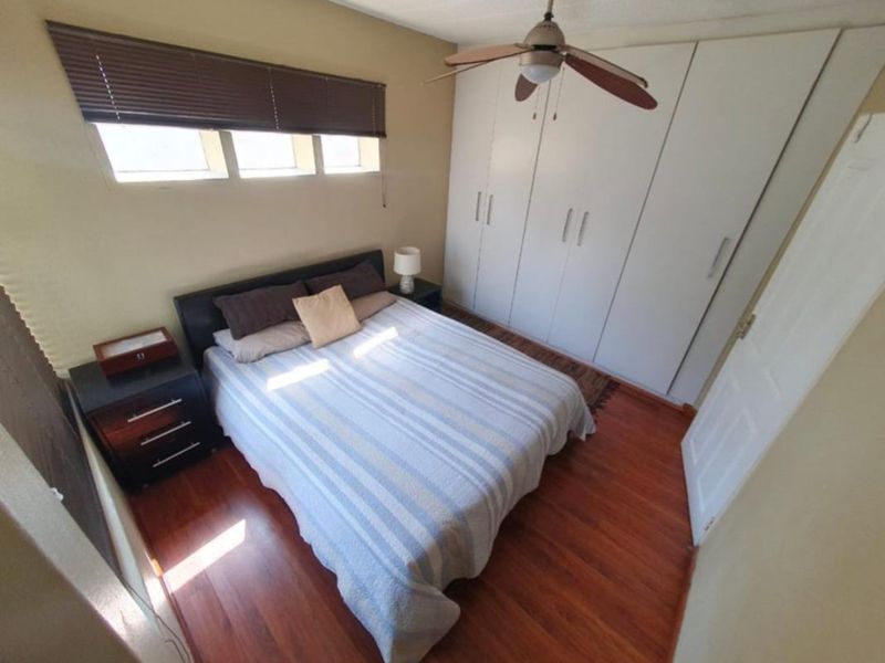 A bedroom featuring laminate flooring, built-in cupboards, a ceiling fan, and horizontal window blinds.