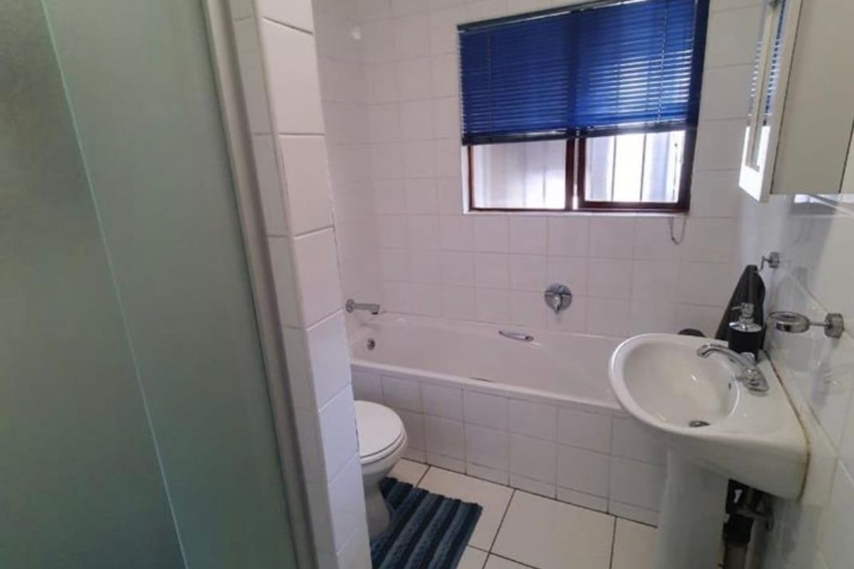 A functional bathroom featuring a bathtub, pedestal basin, and separate shower enclosure with white wall and floor tiling.