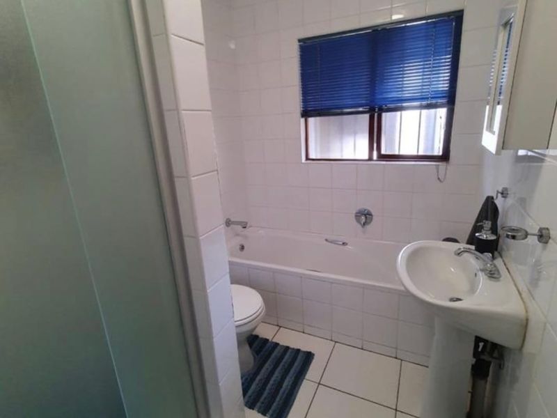 A functional bathroom featuring a bathtub, pedestal basin, and separate shower enclosure with white wall and floor tiling.
