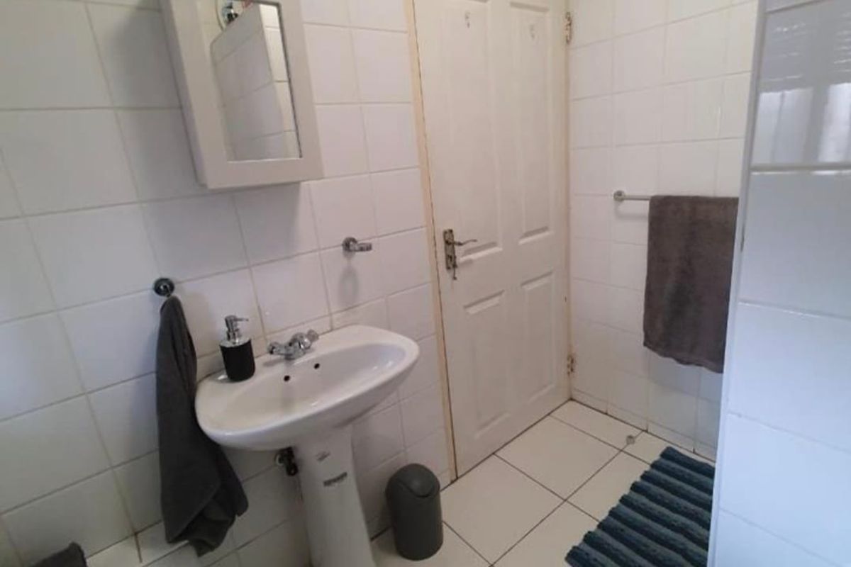 A functional bathroom featuring a pedestal basin, bathtub, and white wall tiling throughout, offering a clean and practical layout.