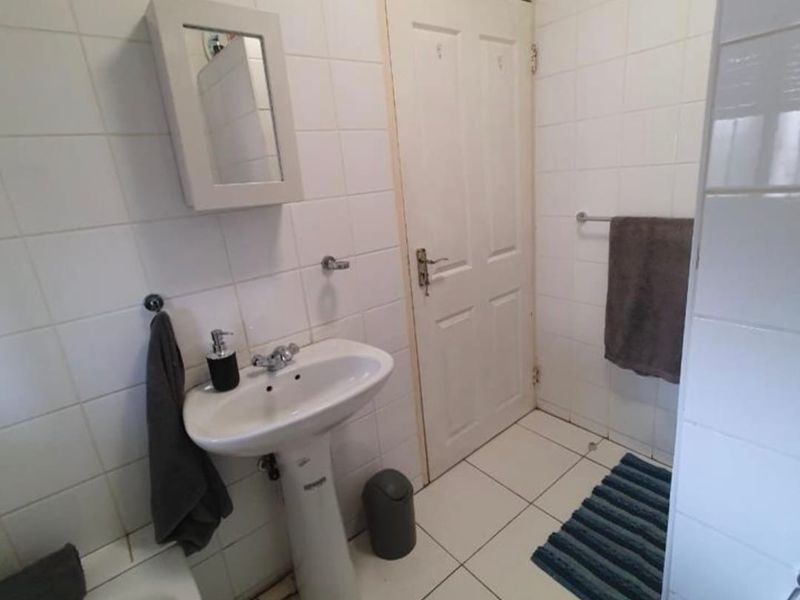 A functional bathroom featuring a pedestal basin, bathtub, and white wall tiling throughout, offering a clean and practical layout.