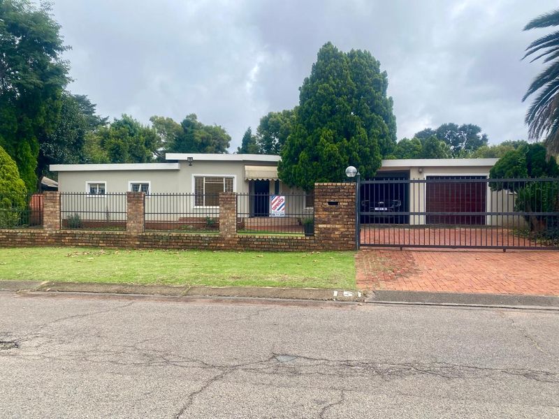 Front view of a single-story house featuring a brick boundary wall, metal security fencing, and a paved driveway leading to a double garage.