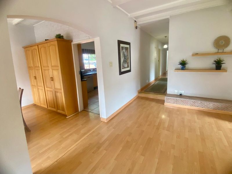 Living area featuring light laminate flooring, a decorative archway, and a tiled hearth, with a view through to the kitchen and hallway.