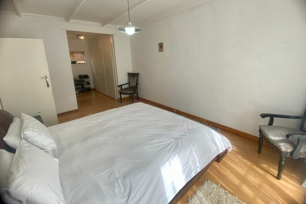 A bedroom featuring laminate flooring, built-in cupboards, and a neutral color palette, offering a functional space with direct access to an adjoining area.