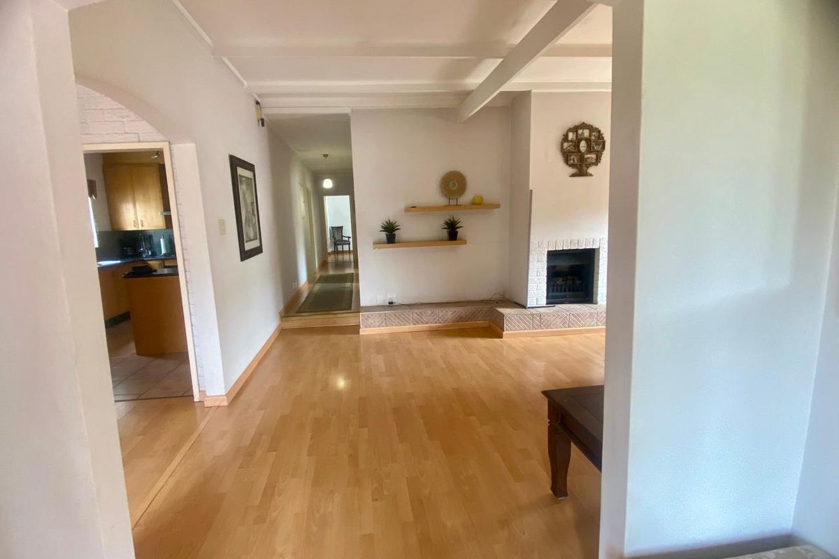 Spacious living room featuring laminate flooring, exposed ceiling beams, and a fireplace with a tiled hearth, leading into a kitchen and hallway.