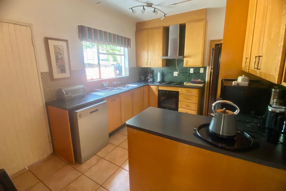 A functional kitchen featuring wooden cabinetry, dark countertops, a built-in oven with extractor fan, and tiled flooring.